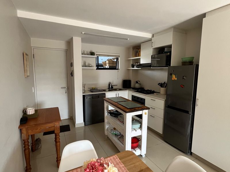 An open-plan kitchen and dining area featuring white cabinetry, tiled flooring, and integrated appliances, providing a functional and well-lit living space.