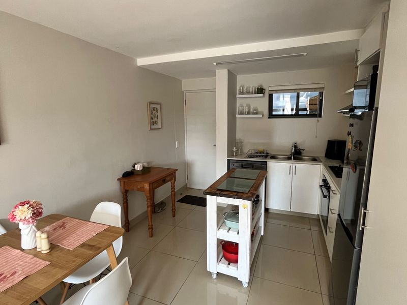 Open-plan kitchen and dining area featuring tiled flooring, modern cabinetry, built-in oven, and functional workspace with floating shelving.