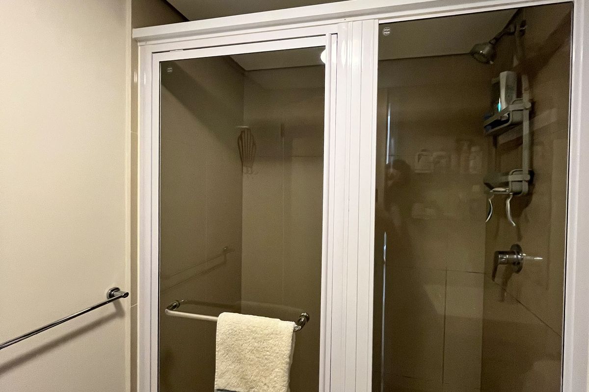 A functional bathroom shower enclosure featuring a tiled floor, glass door, and integrated shower fixtures with an overhead extractor fan.