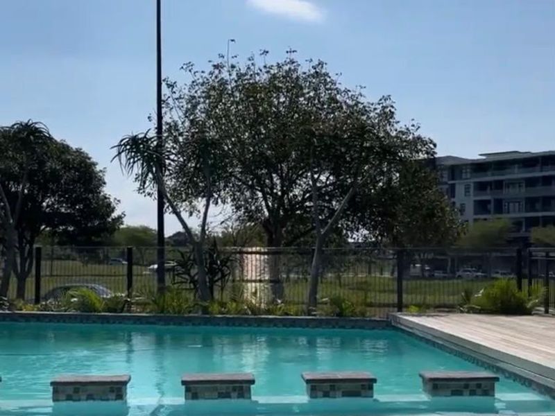 A well-maintained swimming pool area featuring timber decking, built-in pool stools, and secure metal perimeter fencing.