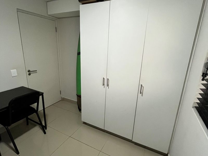 A bedroom featuring neutral tiled flooring and a large white built-in wardrobe providing ample storage space.