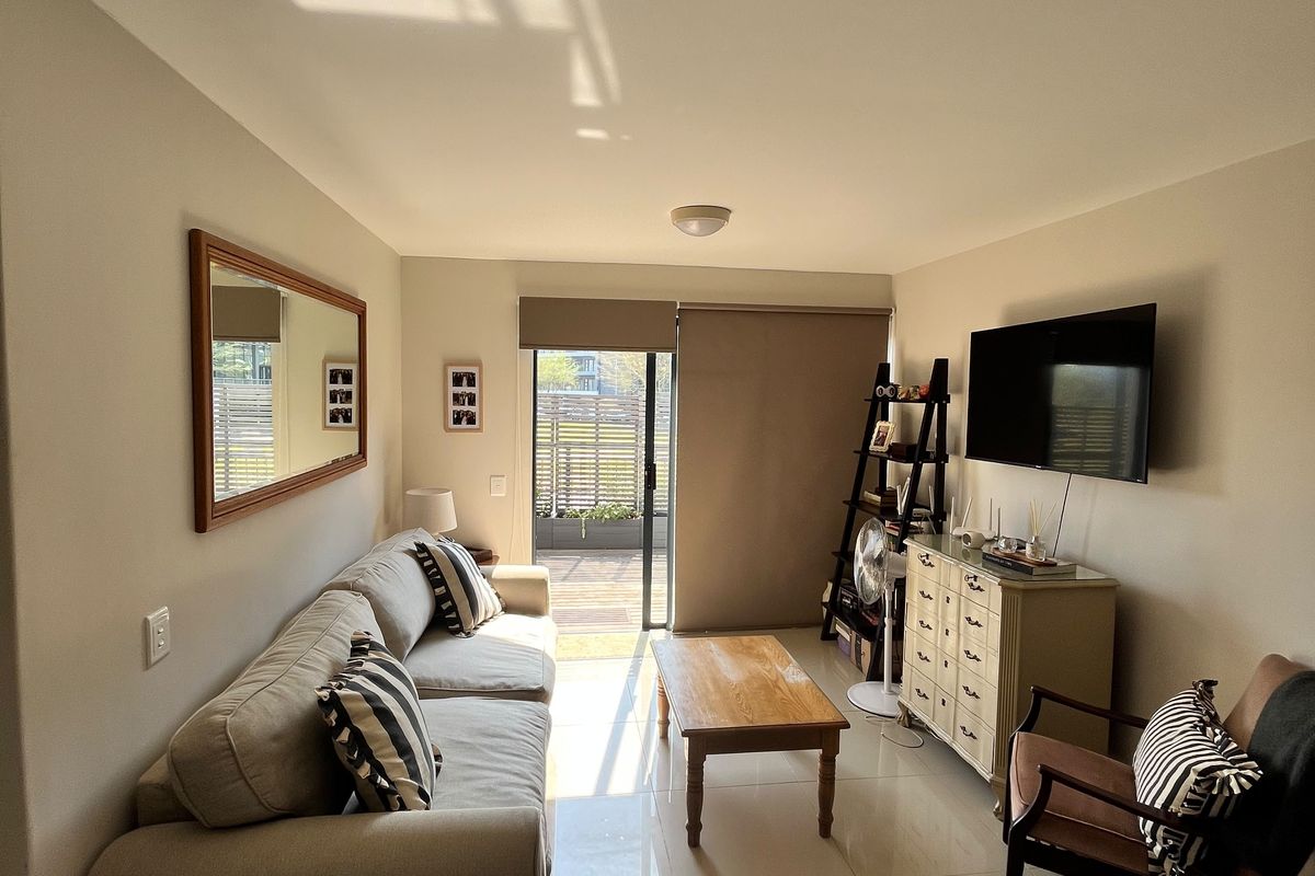 A bright living room featuring large format floor tiles, neutral wall tones, and a sliding glass door providing access to an outdoor patio area.