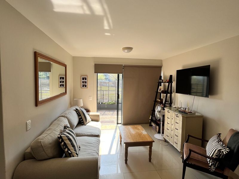 A bright living room featuring large format floor tiles, neutral wall tones, and a sliding glass door providing access to an outdoor patio area.