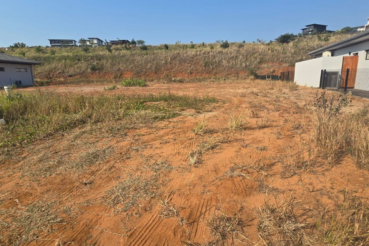 An undeveloped residential plot of land featuring natural terrain and perimeter fencing, situated between existing neighboring properties.