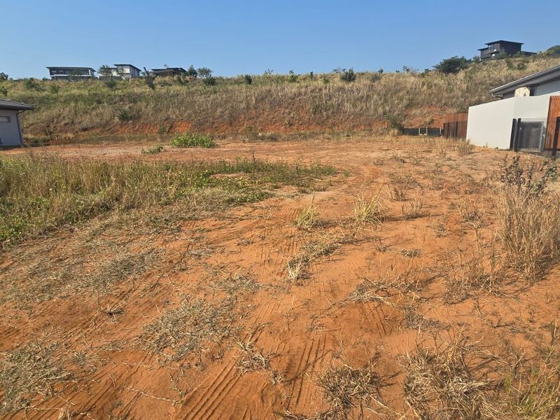 An undeveloped residential plot of land featuring natural terrain and perimeter fencing, situated between existing neighboring properties.