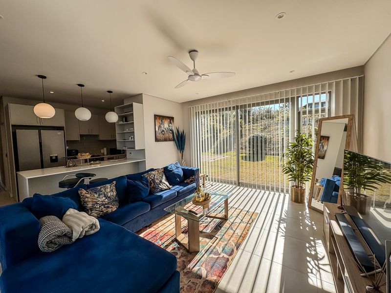A bright open-plan living and kitchen area featuring modern cabinetry, a kitchen island, tiled floors, and large sliding doors leading to the garden.