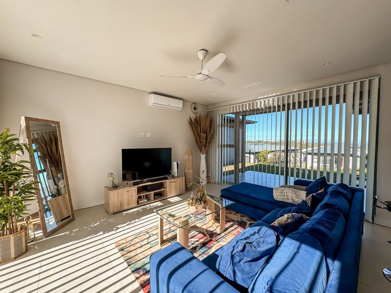 Bright and modern living room featuring tiled flooring, a ceiling fan, split-system air conditioning, and large sliding glass doors leading to an outdoor area.