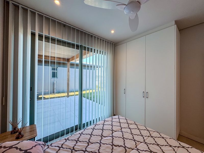 A bright bedroom featuring built-in cupboards, a ceiling fan, and large sliding glass doors that open onto a paved patio area.