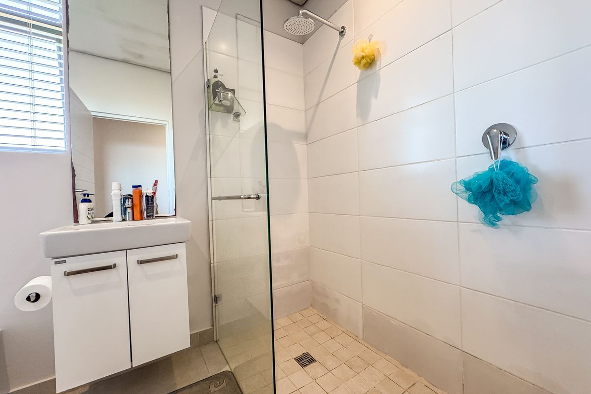 A functional bathroom featuring a wall-mounted vanity, a glass-enclosed shower with a rain shower head, and neutral wall tiling.