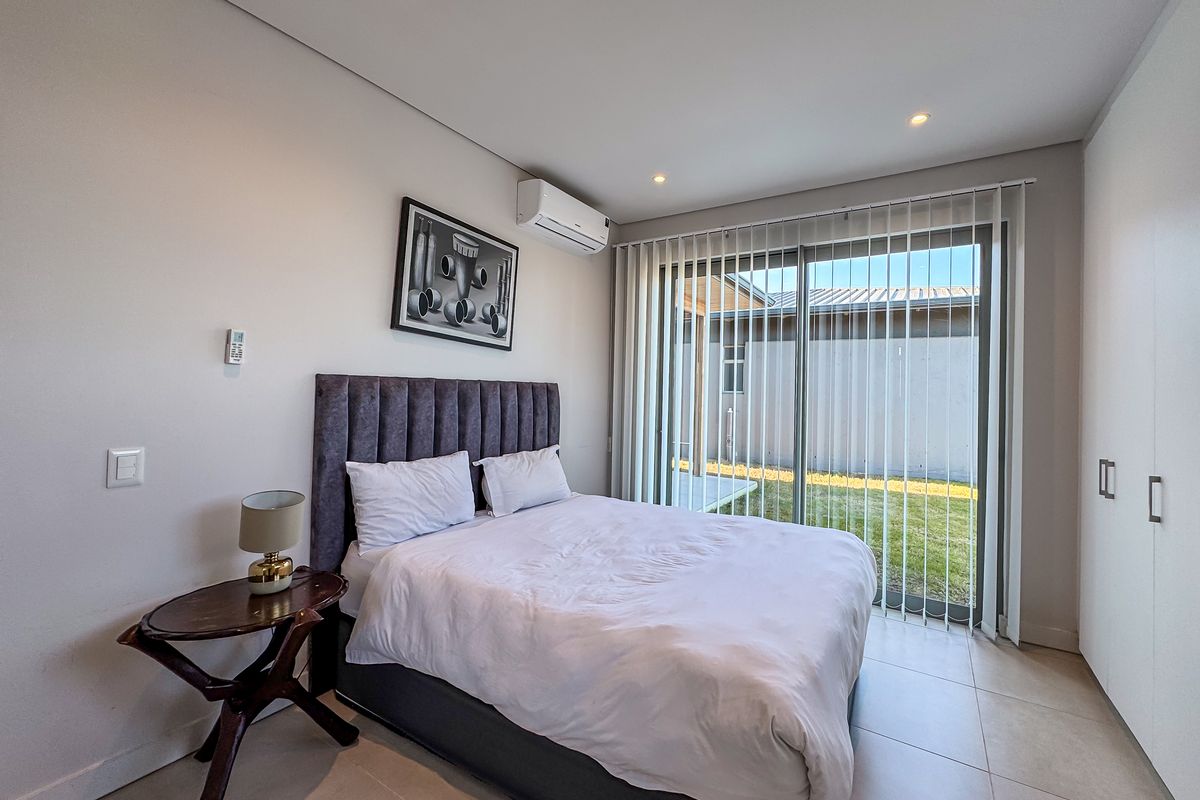 A modern bedroom featuring tiled flooring, a split-system air conditioner, built-in wardrobes, and a sliding glass door providing direct access to the rear garden.