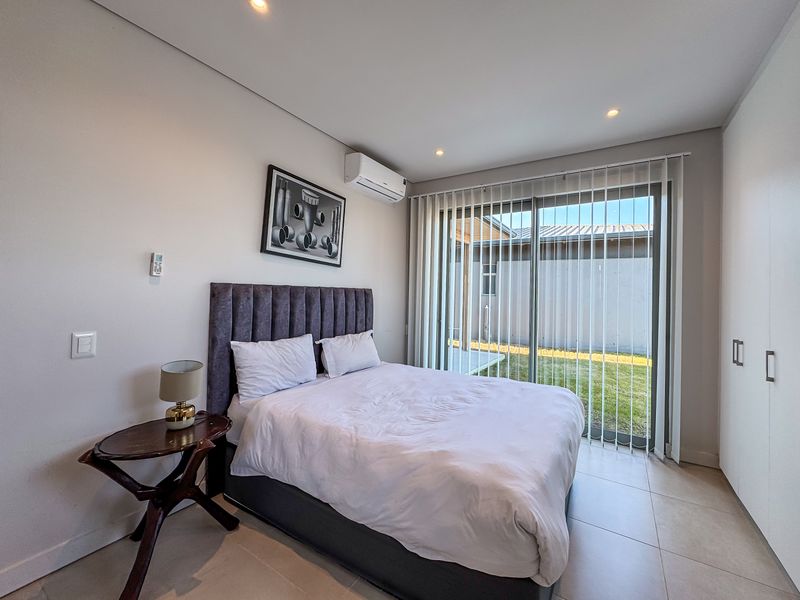 A modern bedroom featuring tiled flooring, a split-system air conditioner, built-in wardrobes, and a sliding glass door providing direct access to the rear garden.