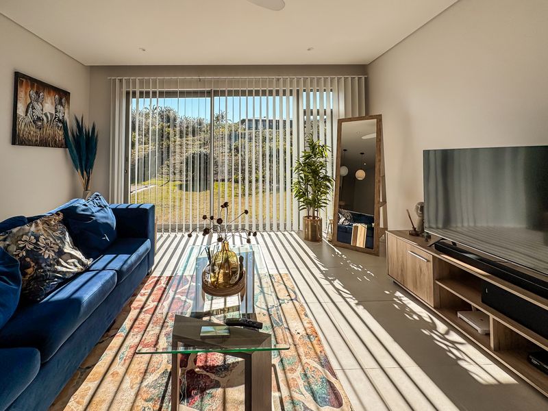 A bright and modern living room featuring large sliding glass doors with vertical blinds, tiled flooring, and recessed ceiling lighting.