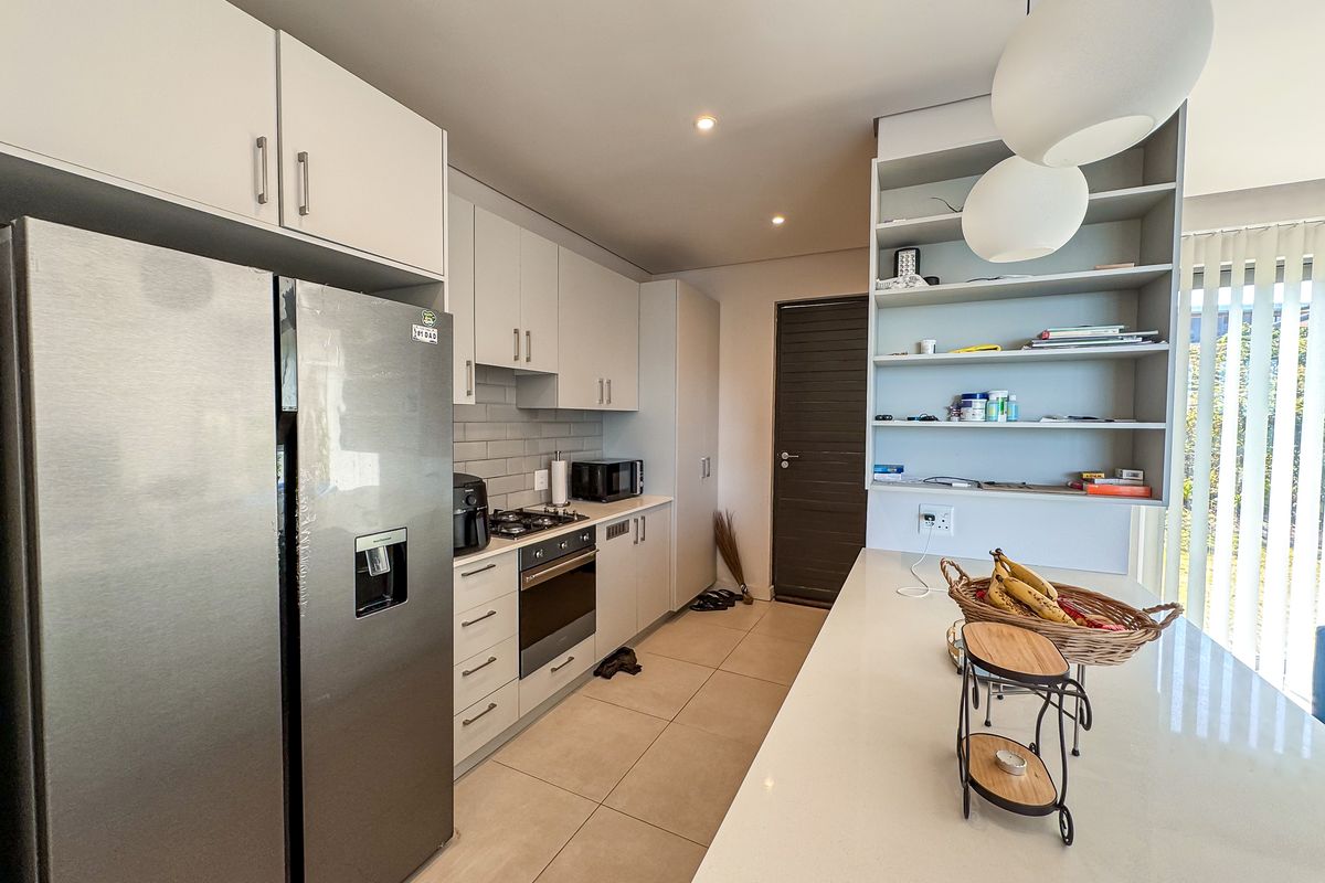 Modern kitchen featuring sleek cabinetry, stone countertops, a gas hob, built-in oven, and a functional breakfast bar with open shelving.