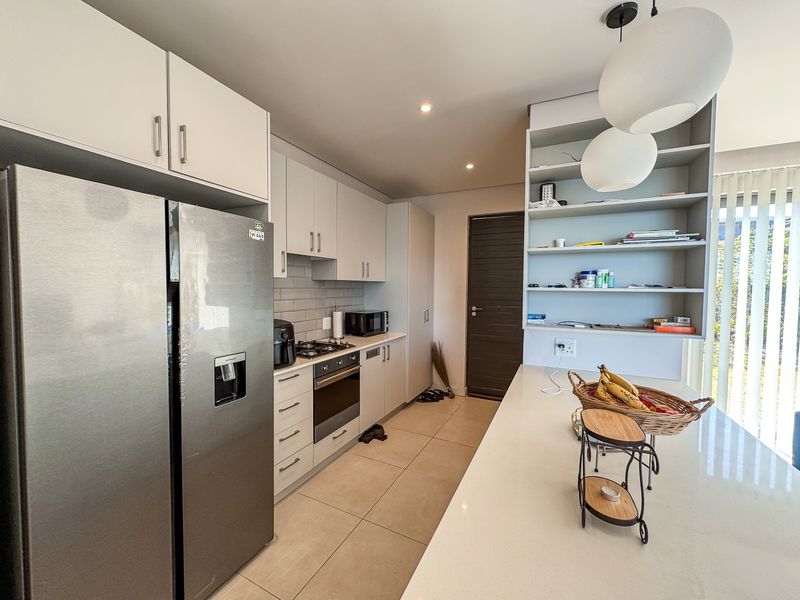 Modern kitchen featuring sleek cabinetry, stone countertops, a gas hob, built-in oven, and a functional breakfast bar with open shelving.