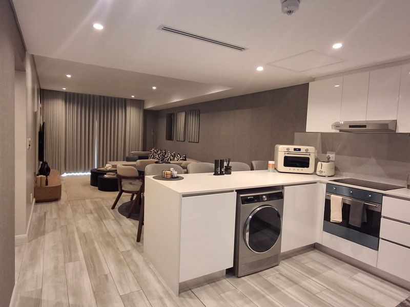 Modern open-plan living area featuring a sleek kitchen with integrated appliances, stone countertops, and contemporary finishes, seamlessly flowing into the lounge space.