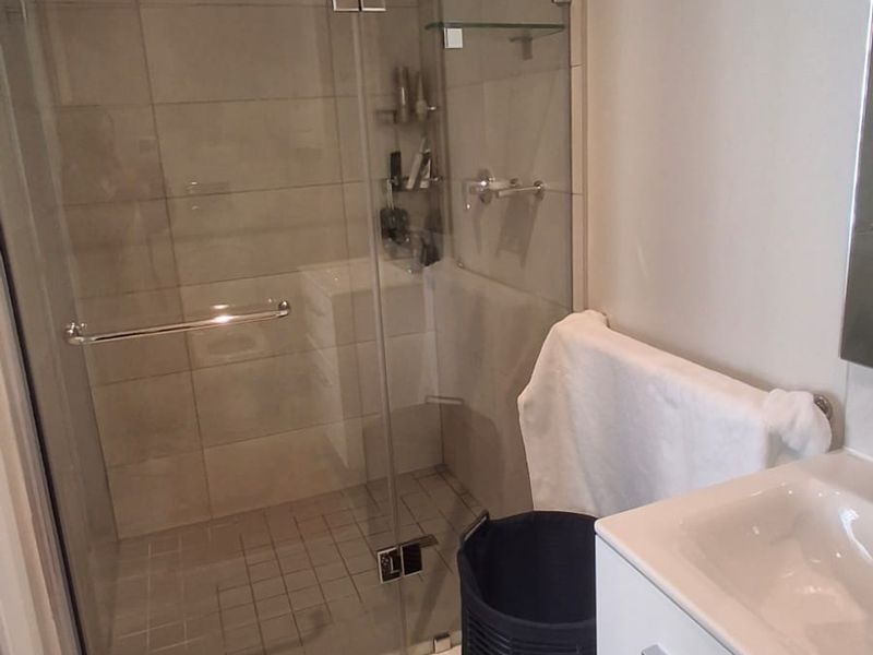 Modern bathroom featuring a glass-enclosed shower with tiled walls and a sleek white vanity cabinet with an integrated sink.