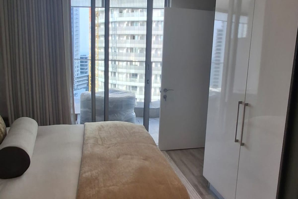 Modern bedroom featuring a built-in wardrobe, recessed lighting, and floor-to-ceiling glass doors providing access to a balcony with urban views.