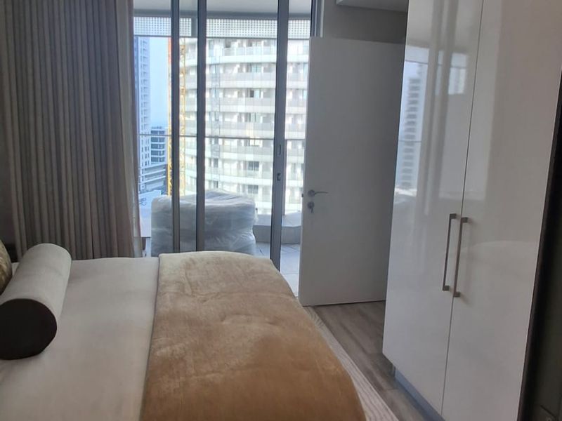 Modern bedroom featuring a built-in wardrobe, recessed lighting, and floor-to-ceiling glass doors providing access to a balcony with urban views.