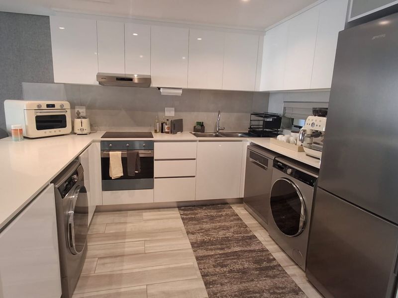 Modern kitchen featuring sleek white cabinetry, stone countertops, integrated appliances, and high-quality finishes in a clean, contemporary layout.