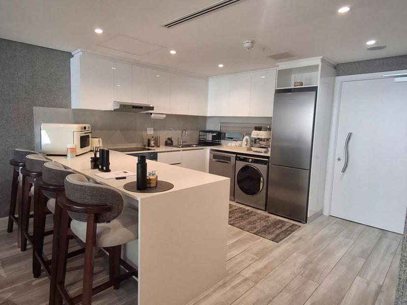 Modern kitchen featuring sleek white cabinetry, stone countertops, a breakfast bar, and integrated appliances including a dishwasher and washing machine.