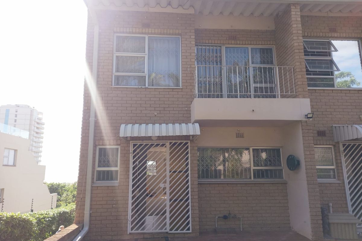 Rear elevation of a face brick townhouse featuring a ground floor patio, security gates, and an upper-level balcony with metal railings.
