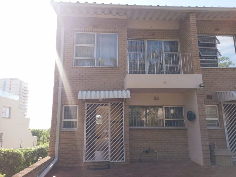 Rear elevation of a face brick townhouse featuring a ground floor patio, security gates, and an upper-level balcony with metal railings.