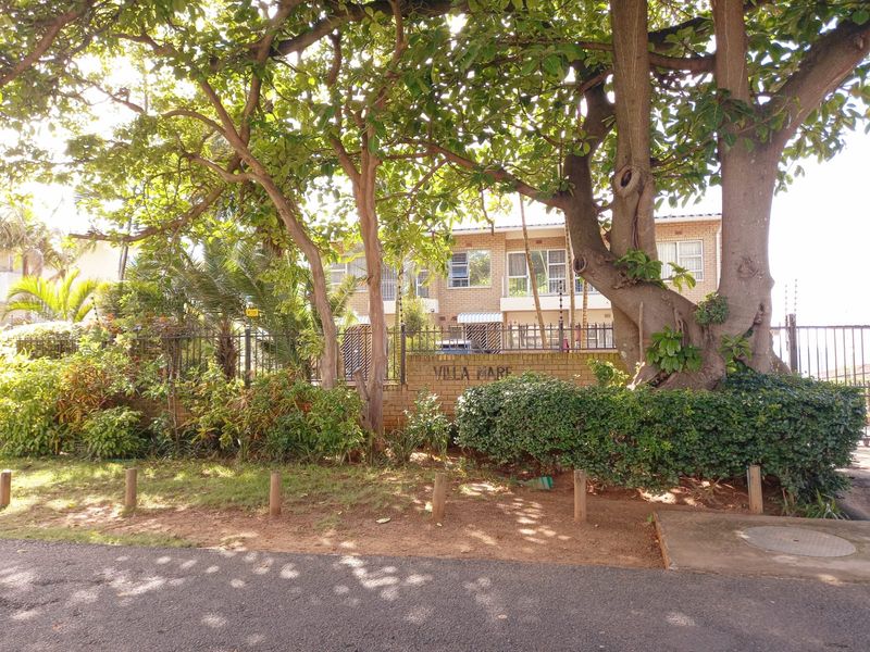 Front exterior view of the Villa Mare townhouse complex, featuring a brick boundary wall, electric fencing, and mature landscaping.