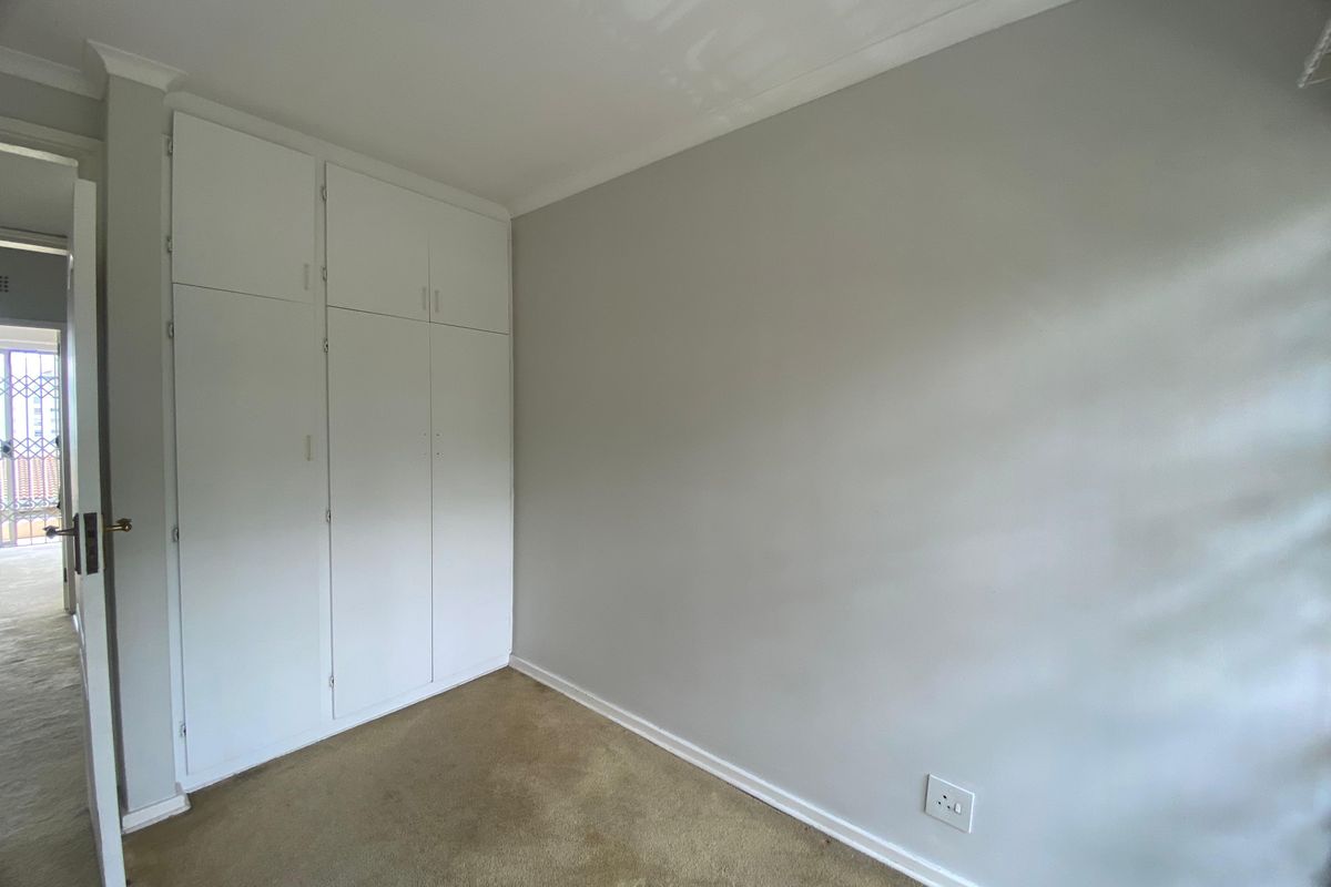 A clean, empty bedroom featuring neutral wall paint, carpeted flooring, and built-in storage cupboards.