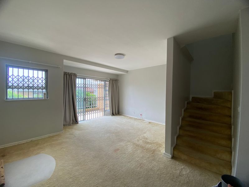 An empty living room featuring carpeted flooring, a staircase, and security gates on the windows and sliding door leading to the exterior.