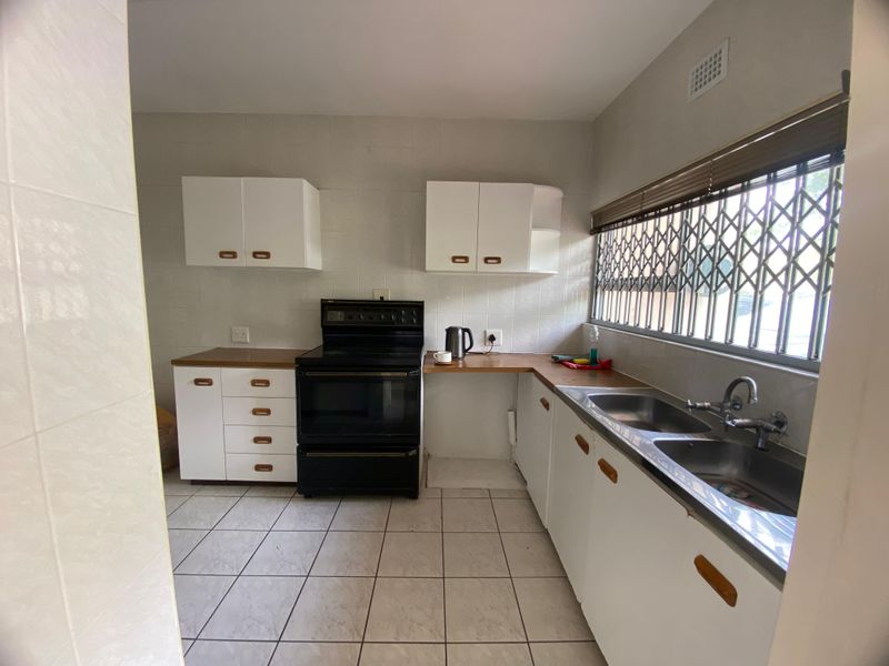 A functional kitchen featuring white cabinetry, a double bowl stainless steel sink, tiled flooring, and a freestanding stove with a security-fitted window.