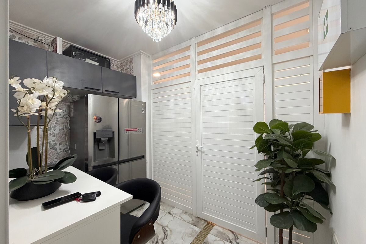Modern kitchen area featuring marble-look flooring, sleek dark cabinetry, and a decorative chandelier, complemented by a unique louvered partition wall.