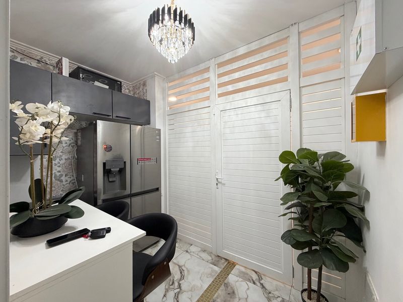 Modern kitchen area featuring marble-look flooring, sleek dark cabinetry, and a decorative chandelier, complemented by a unique louvered partition wall.