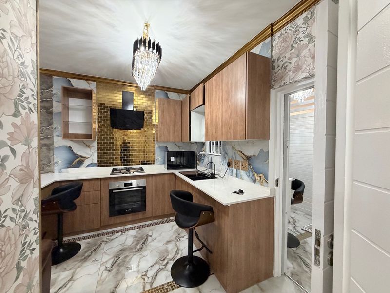 Modern kitchen featuring wood-finish cabinetry, stone countertops, built-in oven, gas hob, and decorative marble-effect wall and floor tiling.