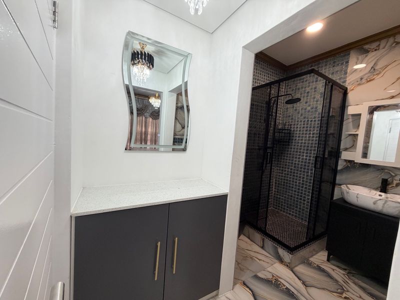 Modern bathroom featuring a sleek vanity with stone countertop, vessel sink, and a contemporary glass-enclosed shower with mosaic tile accents.