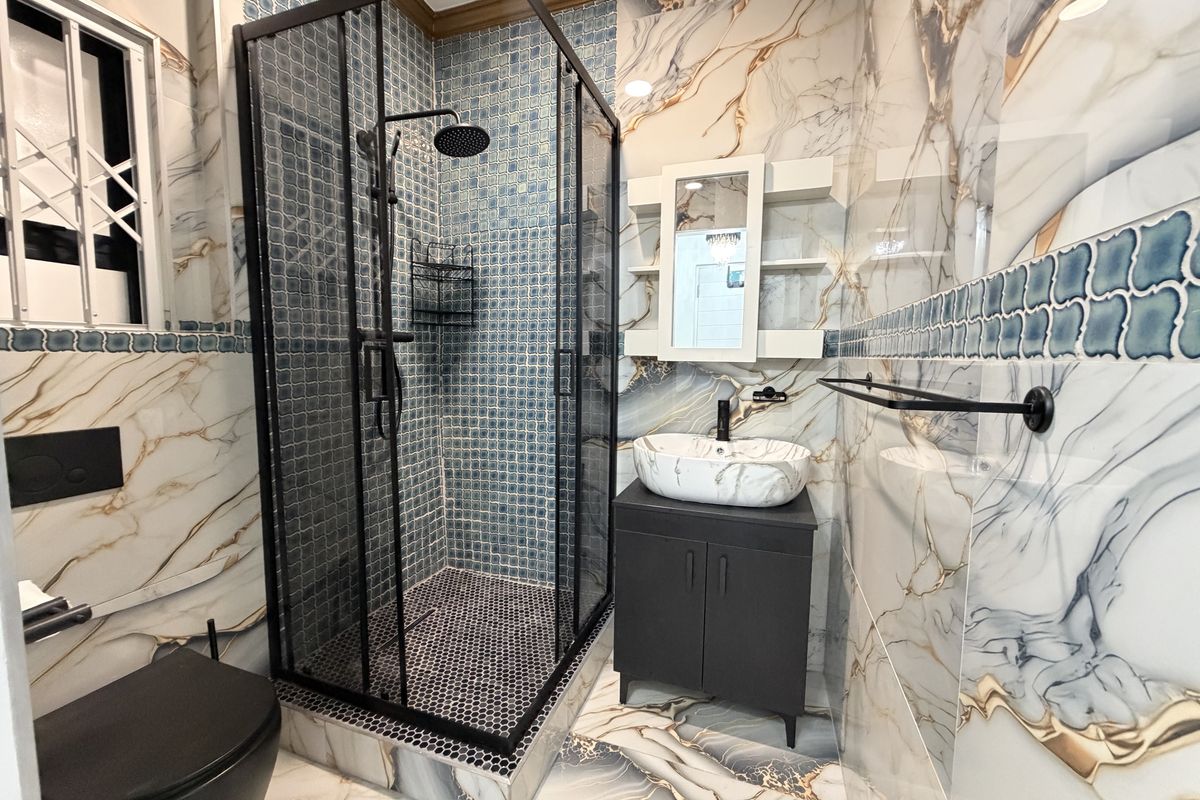 Modern bathroom featuring a walk-in shower with black frame, vessel sink vanity, wall-mounted toilet, and decorative marble-effect wall and floor tiling.