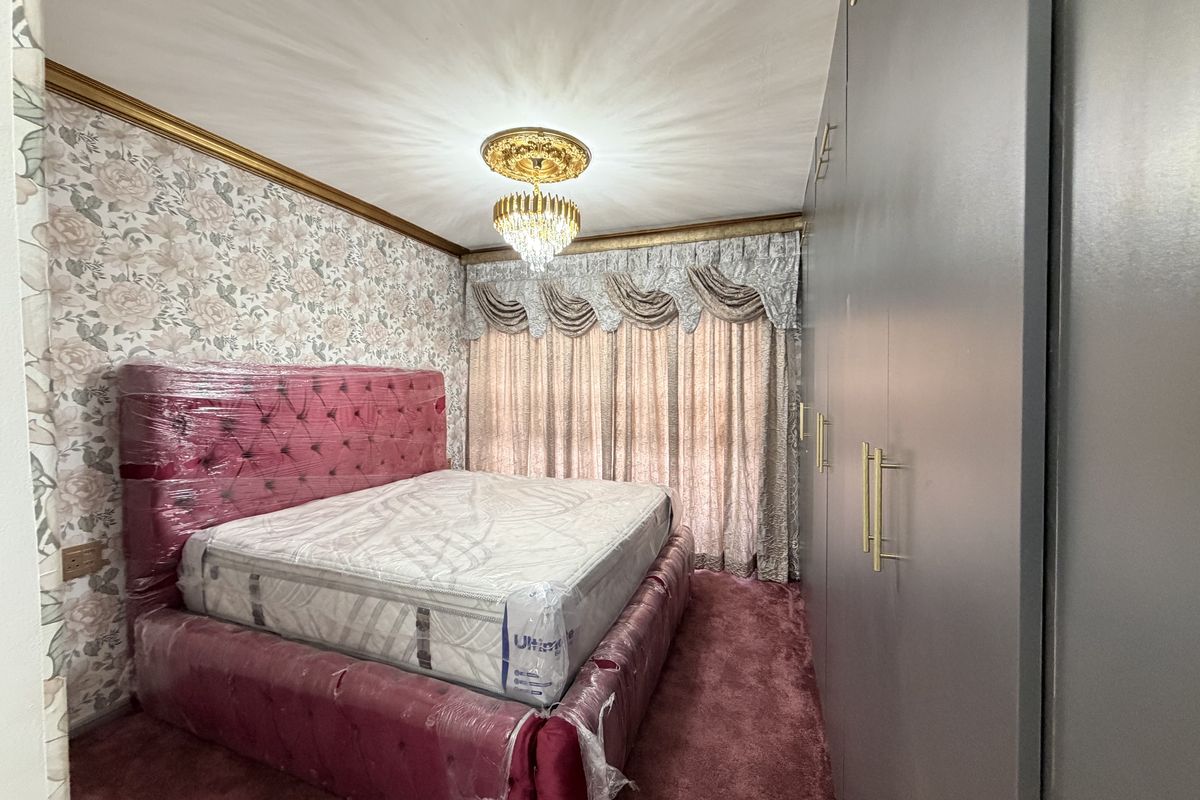 A bedroom featuring built-in wardrobes, a decorative ceiling rose with a crystal chandelier, and floral wallpaper.