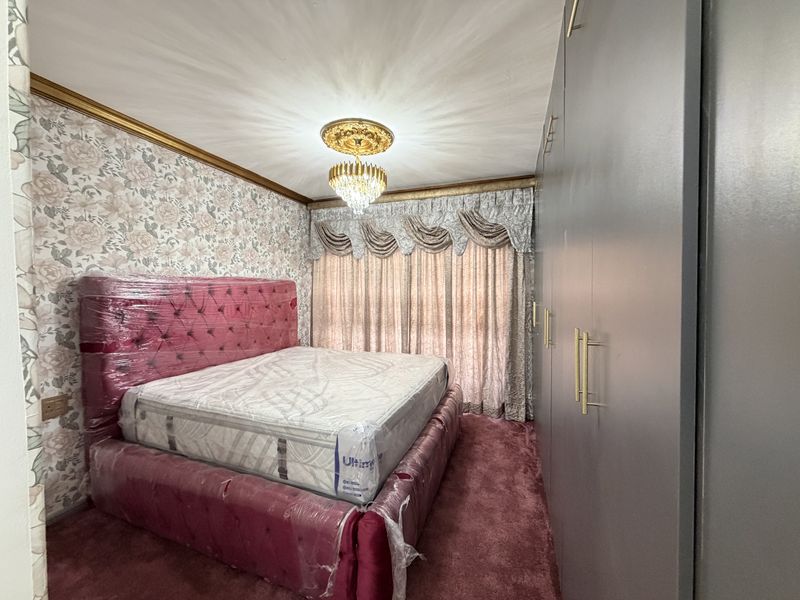 A bedroom featuring built-in wardrobes, a decorative ceiling rose with a crystal chandelier, and floral wallpaper.