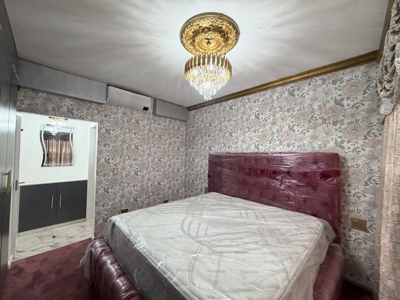 A bedroom featuring floral wallpaper, a decorative crystal chandelier with ceiling rose, and an integrated air conditioning unit, with an adjoining dressing area.