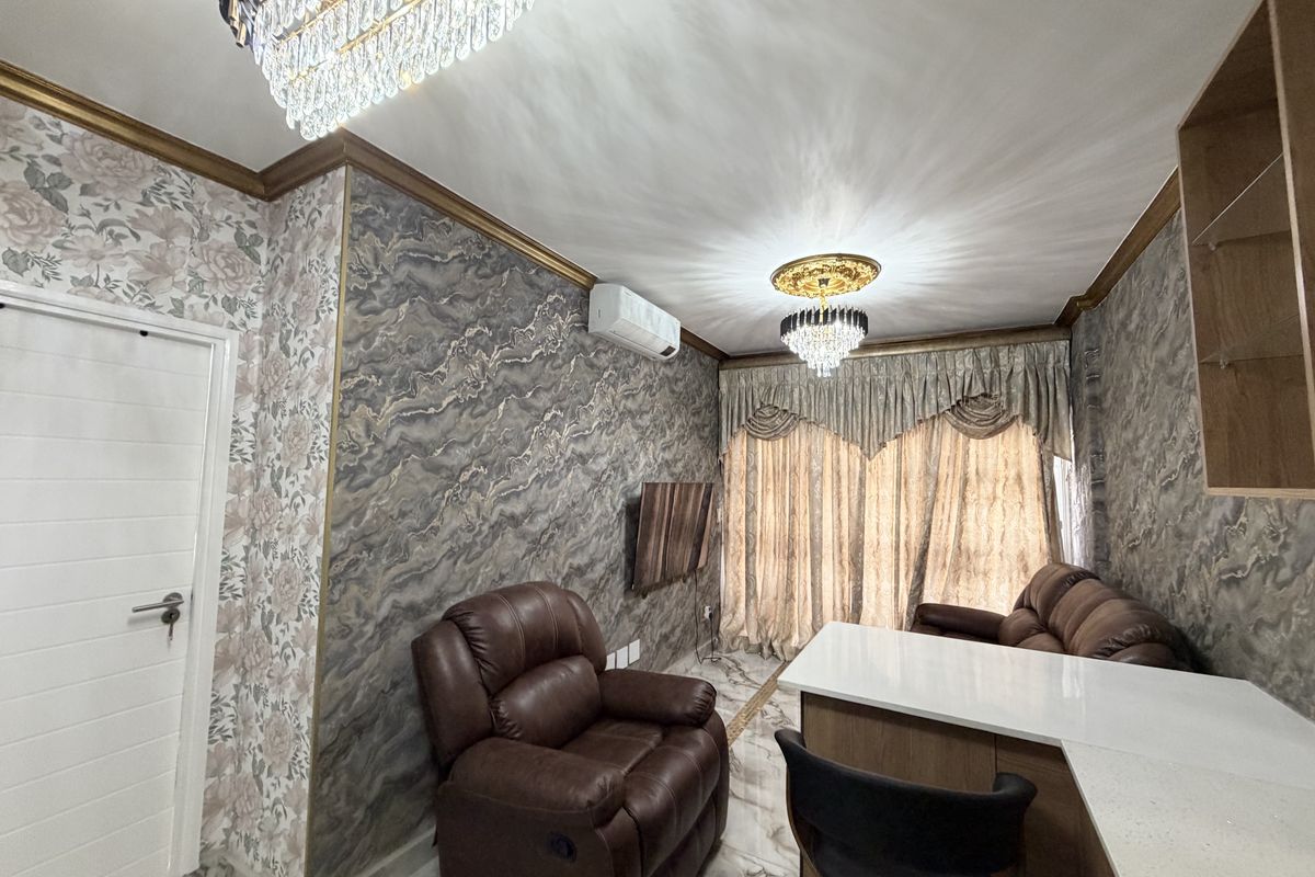 A well-appointed living room featuring marble-effect flooring, decorative crystal chandeliers, ornate ceiling roses, and a wall-mounted split-system air conditioner.