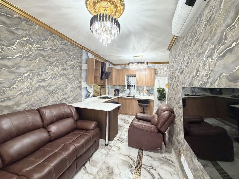 Modern open-plan kitchen and living area featuring marble-effect flooring, custom cabinetry, stone countertops, and decorative lighting fixtures.