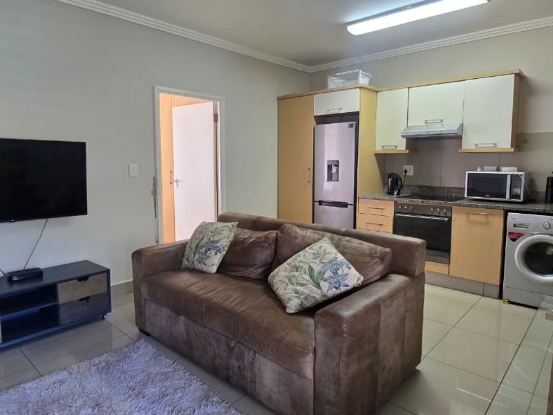 Open-plan living area featuring a compact kitchen with built-in cabinetry, integrated oven, and tiled flooring throughout.