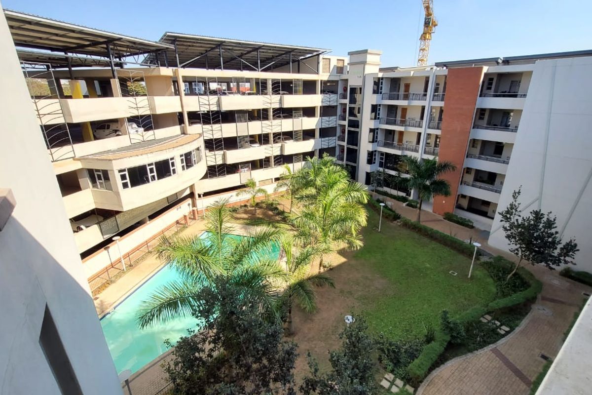 Elevated view of the apartment complex courtyard featuring a swimming pool, landscaped garden, and multi-level parking structure.
