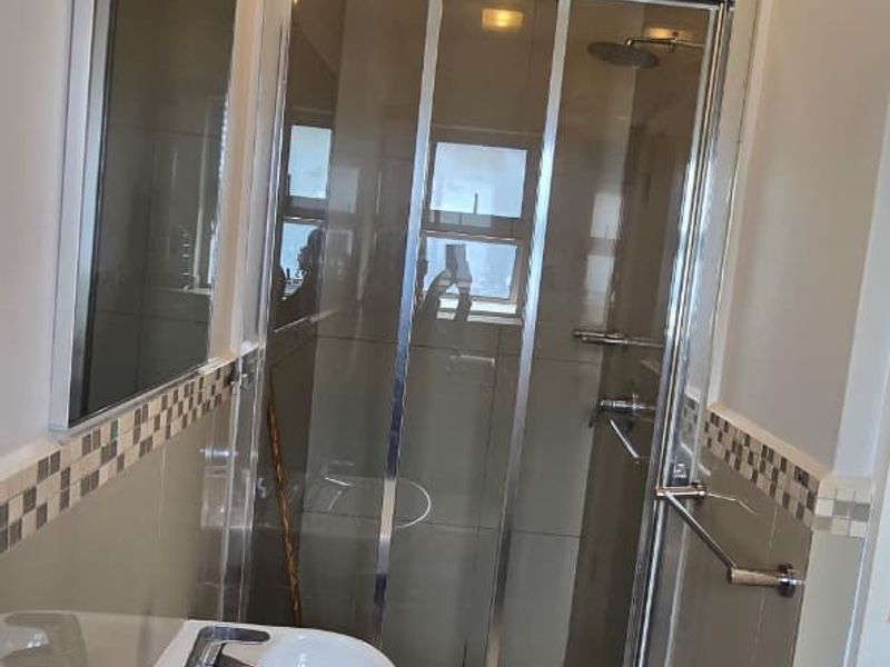 Compact bathroom featuring a wall-mounted basin, chrome fixtures, and a glass-enclosed shower with tiled finishes.