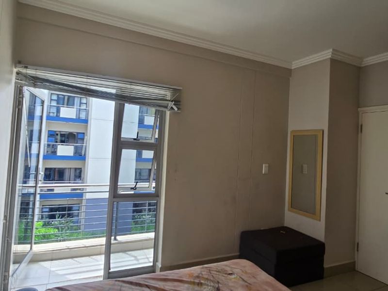 A bedroom featuring built-in cupboards, tiled flooring, and direct access to a private balcony through aluminium-framed doors.