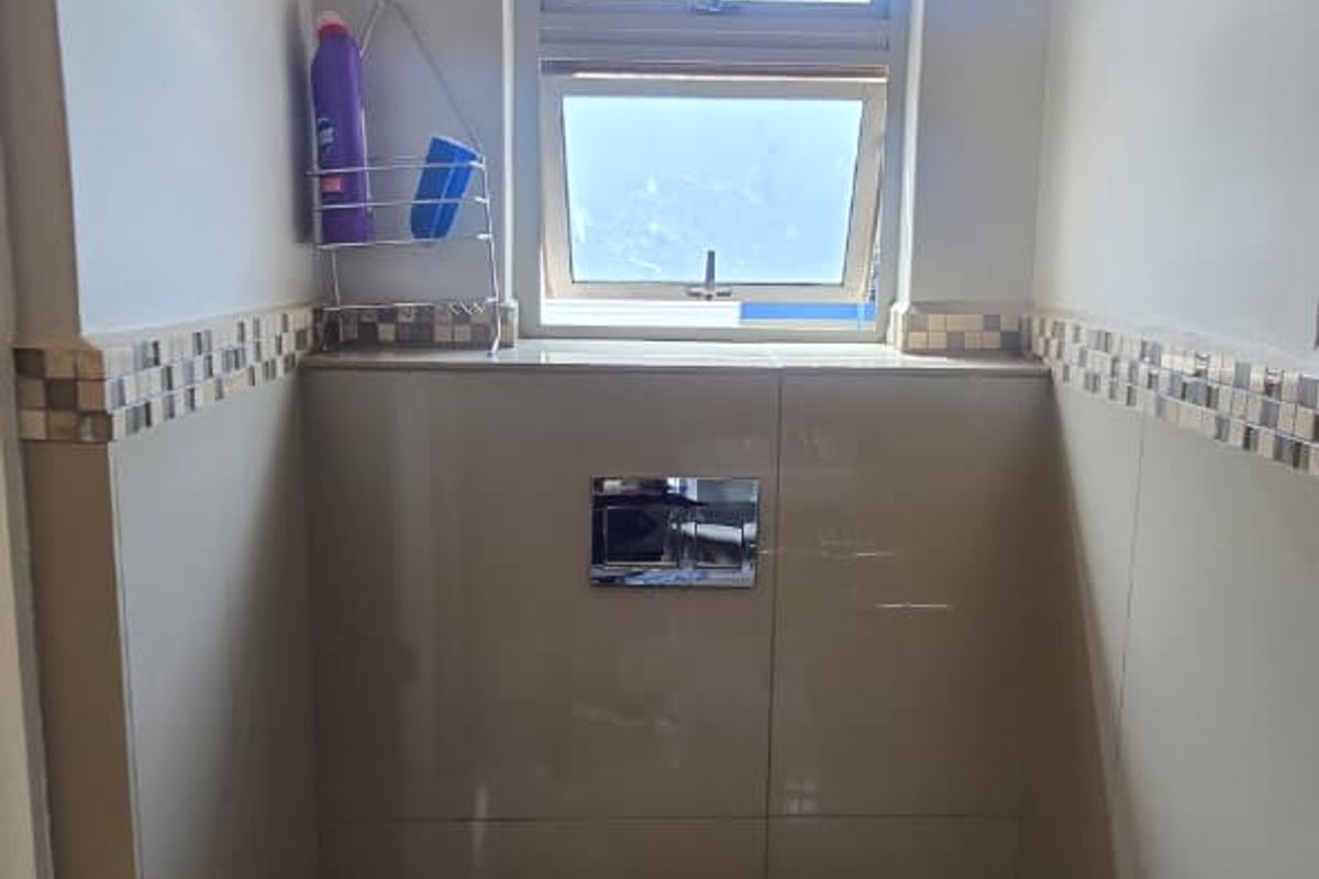 A compact bathroom featuring a wall-mounted toilet with a concealed cistern, neutral wall and floor tiling, and a mosaic tile accent border.