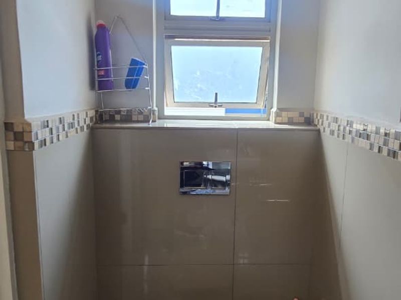 A compact bathroom featuring a wall-mounted toilet with a concealed cistern, neutral wall and floor tiling, and a mosaic tile accent border.