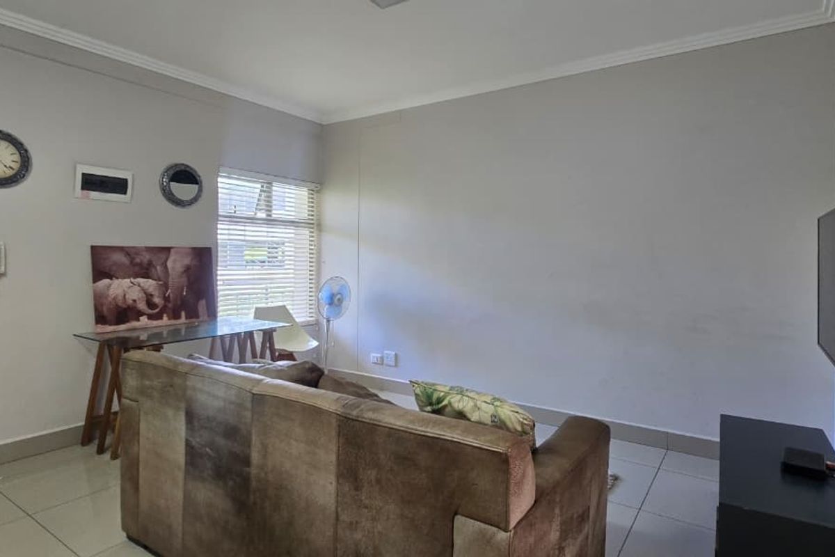 A functional living room featuring tiled flooring, neutral wall finishes, and venetian blinds, providing a clean and simple space for relaxation.