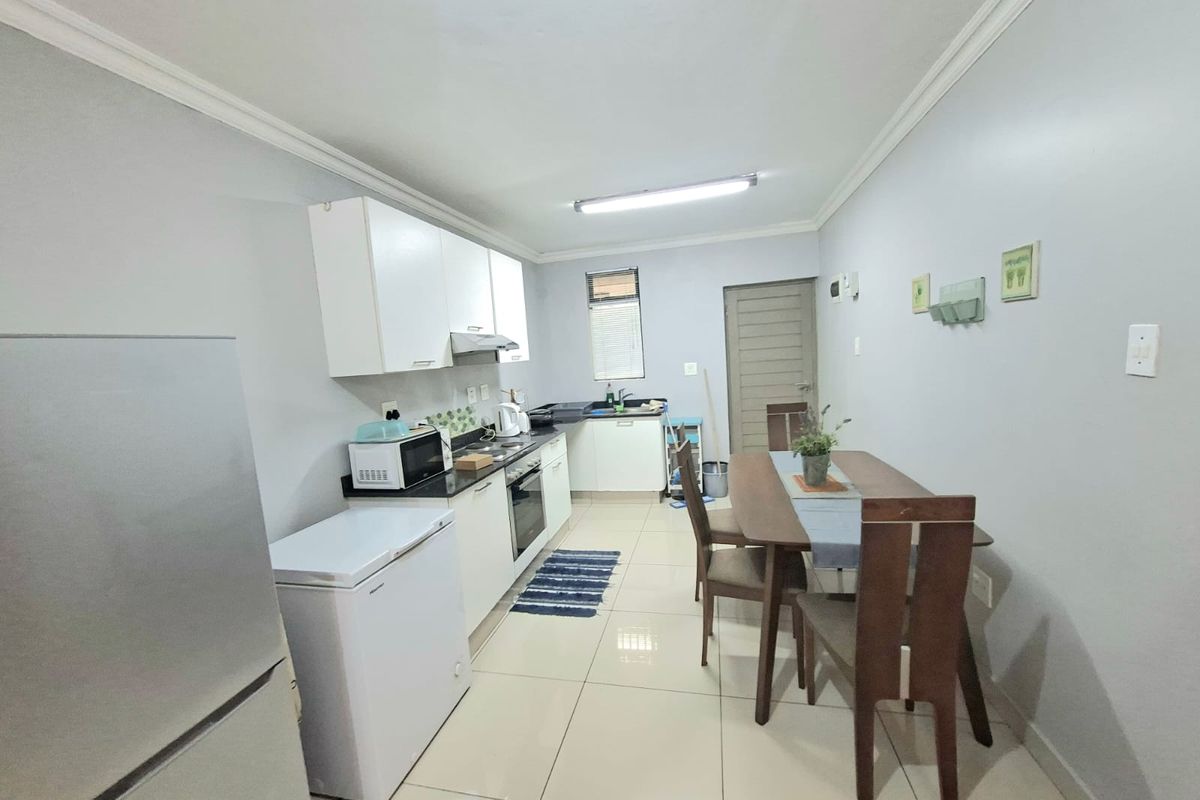 A functional kitchen featuring white cabinetry, dark countertops, built-in oven and hob, and tiled flooring, with an adjacent dining area.