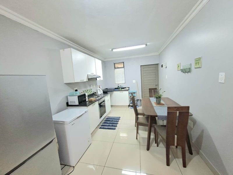 A functional kitchen featuring white cabinetry, dark countertops, built-in oven and hob, and tiled flooring, with an adjacent dining area.
