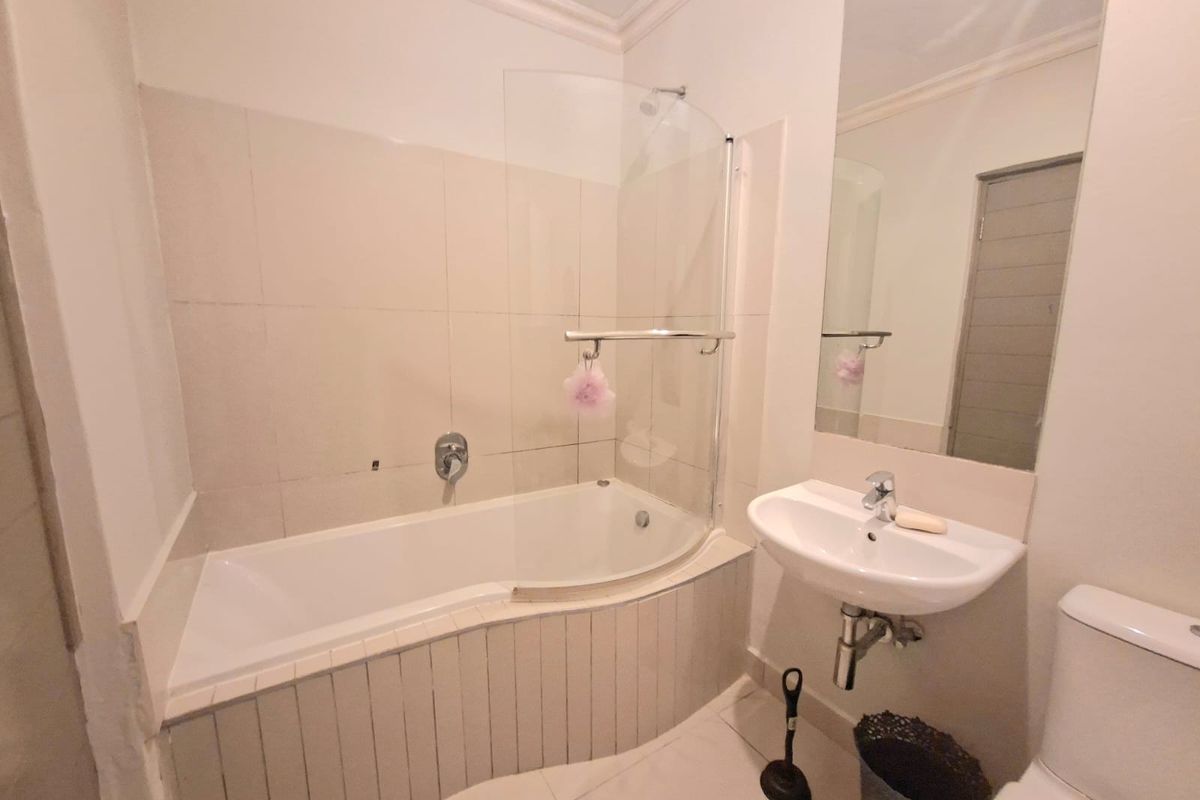 A functional bathroom featuring a bathtub with a glass shower screen, wall-mounted basin, and toilet, finished with neutral wall tiles.